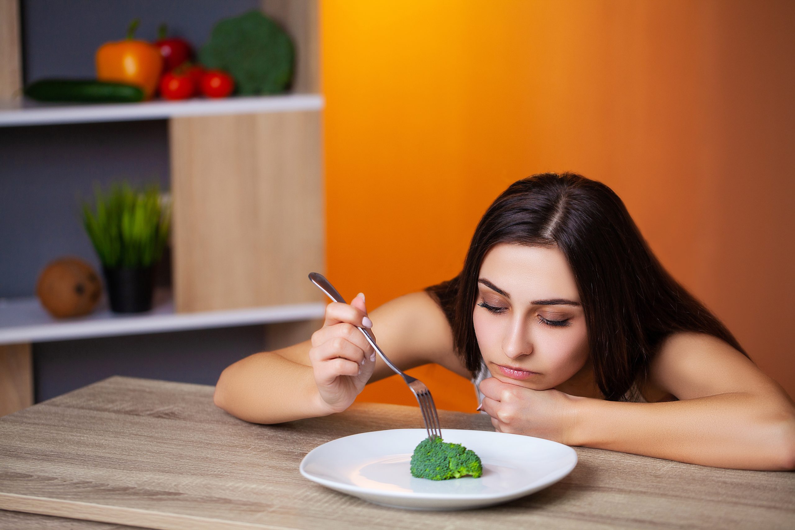 A sad woman stabbing a fork into a single piece of broccoli on a big plate.